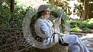 Young beautiful hispanic woman smiling sitting on a bench using smartphone at park