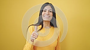 Young beautiful hispanic woman smiling with thumb up over isolated yellow background