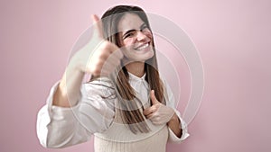 Young beautiful hispanic woman smiling with thumbs up over isolated pink background