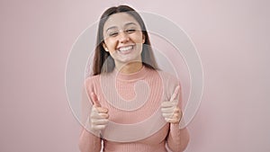 Young beautiful hispanic woman smiling with thumbs up over isolated pink background