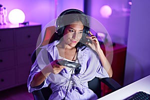 Young beautiful hispanic woman streamer playing video game using joystick at gaming room