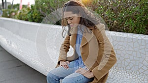 Young beautiful hispanic woman stressed sitting on bench at park