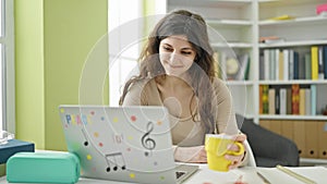 Young beautiful hispanic woman student using laptop drinking coffee at library university