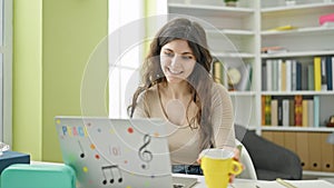 Young beautiful hispanic woman student using laptop drinking coffee at library university