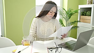 Young beautiful hispanic woman student using laptop reading document at home