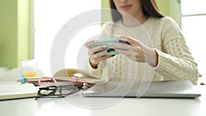 Young beautiful hispanic woman student using smartphone studying at home