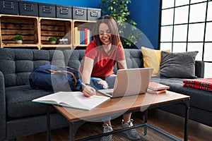 Young beautiful hispanic woman student writing on notebook studying at home