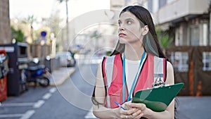 Young beautiful hispanic woman survey interviewer holding clipboard standing with serious expression at street