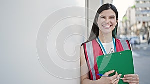 Young beautiful hispanic woman survey interviewer smiling confident holding clipboard at street