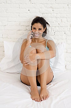 Young beautiful hispanic woman talking relaxed on mobile phone in bed