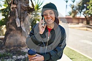Young beautiful hispanic woman talking on smartphone drinking coffee at park