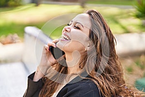 Young beautiful hispanic woman talking on the smartphone sitting on bench at park