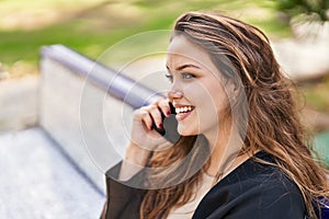 Young beautiful hispanic woman talking on the smartphone sitting on bench at park