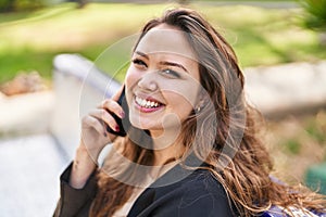 Young beautiful hispanic woman talking on the smartphone sitting on bench at park