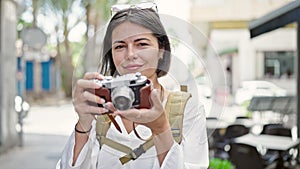 Young beautiful hispanic woman tourist smiling confident using vintage camera at coffee shop terrace