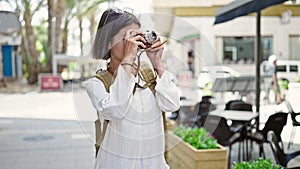 Young beautiful hispanic woman tourist smiling confident using vintage camera at coffee shop terrace