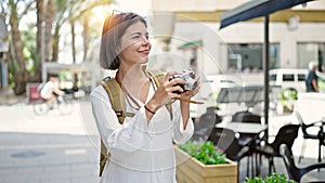 Young beautiful hispanic woman tourist smiling confident using vintage camera at coffee shop terrace