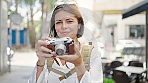 Young beautiful hispanic woman tourist smiling confident using vintage camera at coffee shop terrace