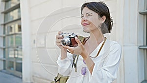 Young beautiful hispanic woman tourist smiling confident using vintage camera at street