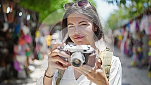 Young beautiful hispanic woman tourist smiling confident using vintage camera at street market