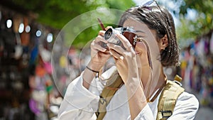Young beautiful hispanic woman tourist using vintage camera at street market