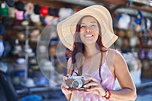 Young beautiful hispanic woman tourist using vintage camera at street market