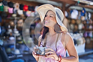 Young beautiful hispanic woman tourist using vintage camera at street market