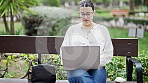 Young beautiful hispanic woman using laptop sitting on a bench at the park