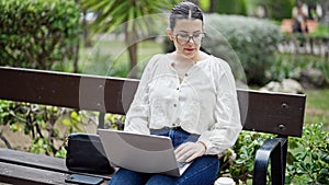 Young beautiful hispanic woman using laptop sitting on a bench at the park