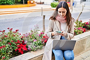 Young beautiful hispanic woman using laptop and smartphone at park