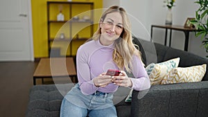 Young beautiful hispanic woman using smartphone doing ok gesture at home