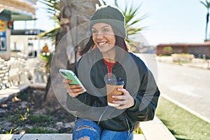 Young beautiful hispanic woman using smartphone drinking coffee at park