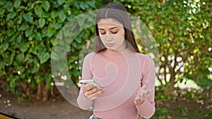 Young beautiful hispanic woman using smartphone with serious expression at park