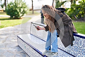 Young beautiful hispanic woman using smartphone sitting on bench at park