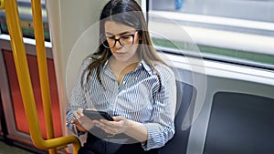 Young beautiful hispanic woman using smartphone sitting on the subway