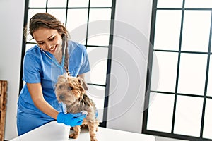 Young beautiful hispanic woman veterinarian examining dog with stethoscope at veterinary clinic