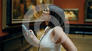 Young beautiful hispanic woman visiting art gallery using smartphone at Art Museum in Vienna