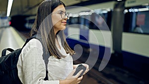 Young beautiful hispanic woman waiting for the subway using smartphone in subway station of Madrid