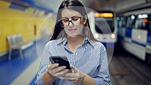 Young beautiful hispanic woman waiting for the subway using smartphone in subway station of Madrid