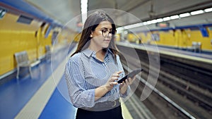 Young beautiful hispanic woman waiting for the subway using smartphone in subway station of Madrid