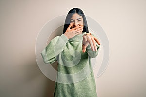 Young beautiful hispanic woman wearing green winter sweater over isolated background laughing at you, pointing finger to the
