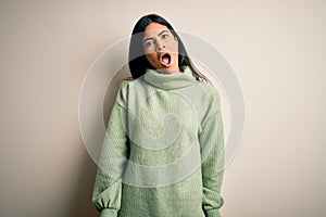 Young beautiful hispanic woman wearing green winter sweater over isolated background In shock face, looking skeptical and