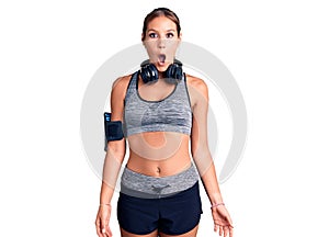 Young beautiful hispanic woman wearing gym clothes and using headphones afraid and shocked with surprise expression, fear and