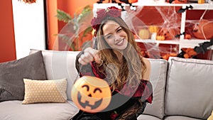 Young beautiful hispanic woman wearing katrina costume holding halloween pumpkin basket at home
