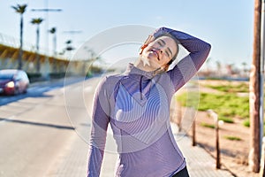 Young beautiful hispanic woman wearing sportswear stretching head at street