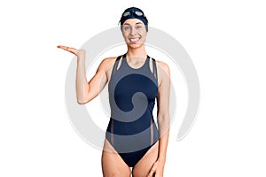 Young beautiful hispanic woman wearing swimwear and swimmer glasses smiling cheerful presenting and pointing with palm of hand
