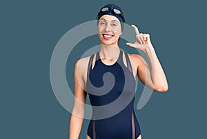 Young beautiful hispanic woman wearing swimwear and swimmer glasses smiling and confident gesturing with hand doing small size