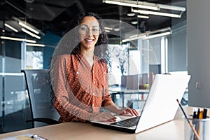 Young beautiful hispanic woman working inside modern office, businesswoman smiling and looking at camera at work using