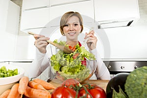 Young beautiful home cook woman at modern kitchen preparing vegetable salad bowl smiling happy