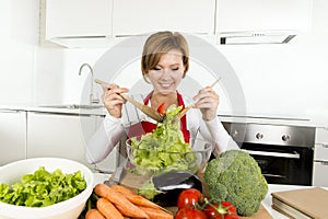 Young beautiful home cook woman at modern kitchen preparing vegetable salad bowl smiling happy